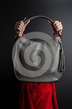 Girl holding a gray leather bag in her outstretched hands on black background, grey bag in female hands side view on black backgro