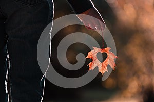 Girl holding in hand leaf with heart during beautiful warm autumn evening, september,love