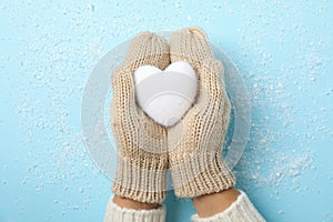 Girl holding in hands white heart on blue background with snow