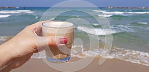 Girl holding in her hand latte coffee in transparent glass against sea waters