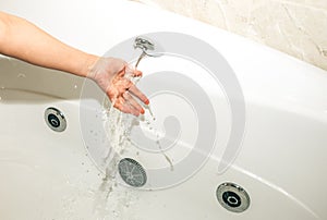 Girl is holding her hand under the water stream in jacuzzi. White bath for relaxation. Water splashes in the spa center