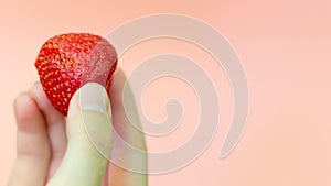 The girl is holding a juicy strawberry on a pink background. strawberry in her hand. Ripe, red strawberries. copy space.