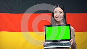 Girl holding laptop with green screen, German flag on background, traveling