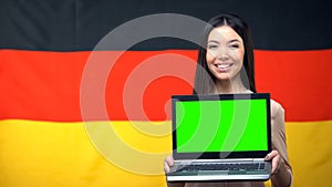 Girl holding laptop with green screen, German flag on background, traveling