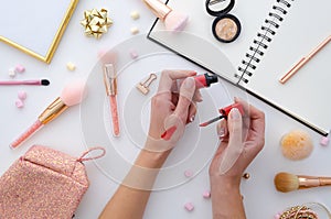 Girl is holding lipstick in hands, makeup swatches,notebook. highlighter,make-up cosmetics on white background. Flat lay