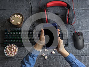 Girl holding a mobile phone on the background of computer accessories, coffee and marshmallows. Black clipping background.