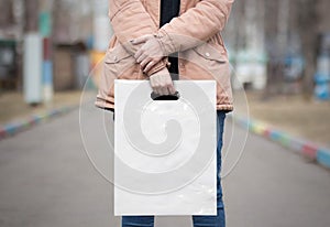 The girl is holding a mockup white plastic bag. A girl with a package on the street in the park