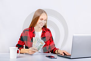 Girl holding money banknotes while sitting with laptop computer.