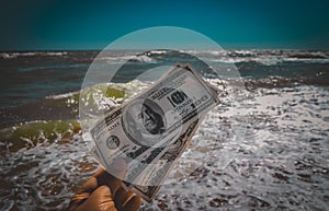 Girl holding a money bill of 300 dollars on background of sea waves