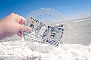 Girl holding a money bill of 300 dollars on background of sea waves