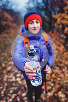 The girl is holding out a bottle of water.