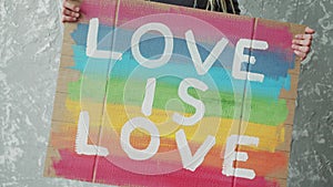 Girl is holding the painting with LGBT pride slogan against homosexual discrimination Love is love