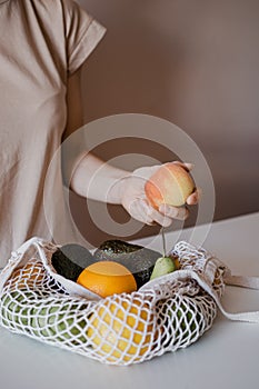 The girl is holding a peach above an eco-aware handbag with a variety of fruits.