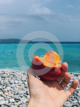 the girl is holding a peach on the background of the blue sky