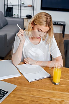 Girl holding pen near notebook, laptop