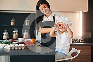 Girl is holding pepper. Mother with her daughter are preparing food on the kitchen