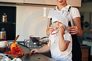 Girl is holding pepper. Mother with her daughter are preparing food on the kitchen