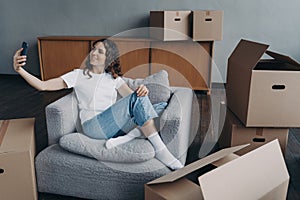 Girl holding phone communicates by video call, showing house with cardboard boxes on moving day