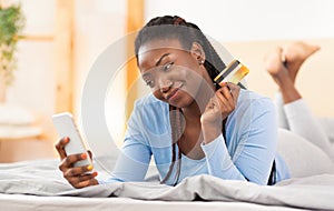 Girl Holding Phone And Credit Card Lying In Bed