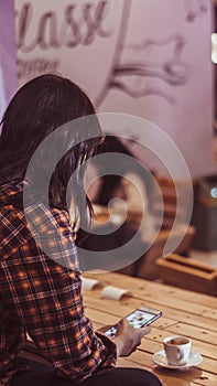 A girl holding phone while enjoying a cup of espresso macchiato in coffee shop