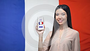 Girl holding phone with learn French application, flag on background, education