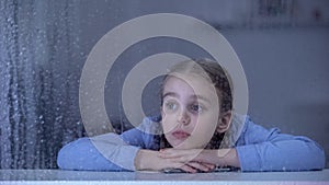 Girl holding phone and lying on window sill, waiting parents from work, rain