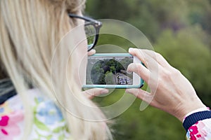 A girl holding a phone to photograph a landscape view.