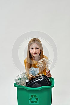 Girl holding plastic bottle from full dustbin