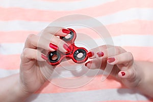 A girl is holding a popular toy metallic red fidget spinner.