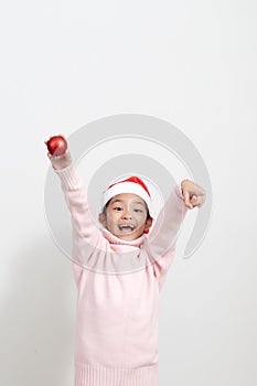 Girl holding a red christmas ball in sweater and santa hat