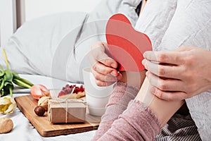 The girl is holding a red heart. Congratulations on Valentine`s Day on February 14. Breakfast in bed and a gift