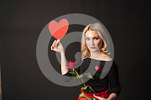 A girl holding a rose and a valentine red heart, a flirting board, on the floor hearts are a lovely space. February 14