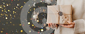 girl holding small gift in her hands. decorated Christmas tree on background. Bright Christmas card with space for text