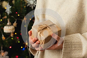 girl holding small gift in her hands. decorated Christmas tree on background.