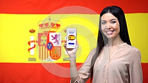 Girl holding smartphone with language study app, Spanish flag on background photo