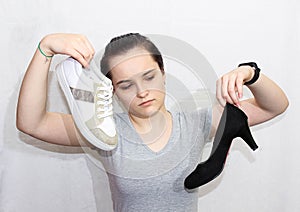 The girl is holding a sneaker and a high-heeled Shoe