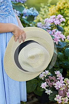Girl is holding a straw hat in a hand in front of Hydrangea bushes Hydrangea macrophylla.