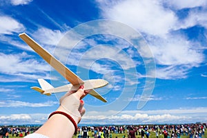 Girl holding toy plane at an airshow with crowd in the background and clear blue sky