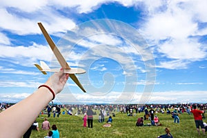 Girl holding toy wood plane at an airshow with crowd in the back