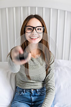 Girl holding a TV remote, changing the channel. Young woman sitting at home with the remote control watching television alone.