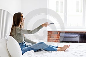 Girl holding a TV remote, changing the channel. Young woman sitting at home with the remote control watching television alone.