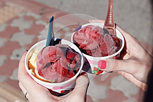 The girl is holding two cups of delicious fruit ice cream, sorbet. Selection of gourmet flavours of ice cream in individual plasti