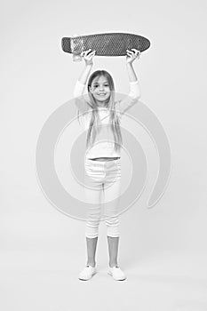 Girl holding violet skateboard above her head. Champion in street race, happy childhood concept. Kid in white jumper