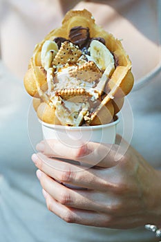 Girl is holding a waffle cone with ice cream, cookies and chocolate sauces in her hand.