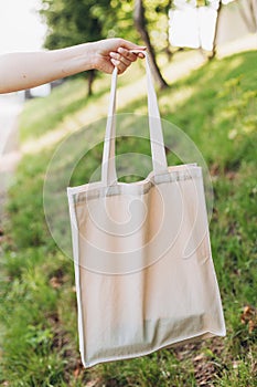 Girl is holding white bag canvas fabric for mockup blank template isolated on nature background. Zero waste concept. Eco