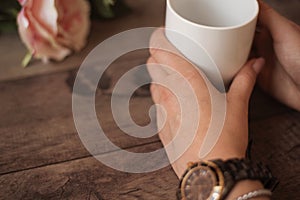 Girl is holding white cup in hands. White mug for woman, gift. Female hands with watch and bracelets holding hot cup of coffee