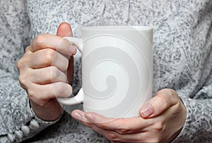 Girl is holding white cup in hands. White mug in woman's hands. photo