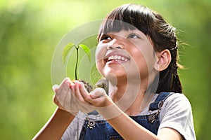 A girl holding a young plant in her hands with a hope of good environment