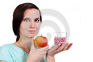 The girl holds apple and vitamins in hand