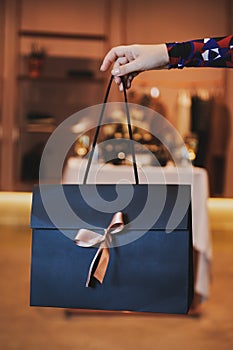 Girl holds beautiful dark blue gift bag with a pink bow.